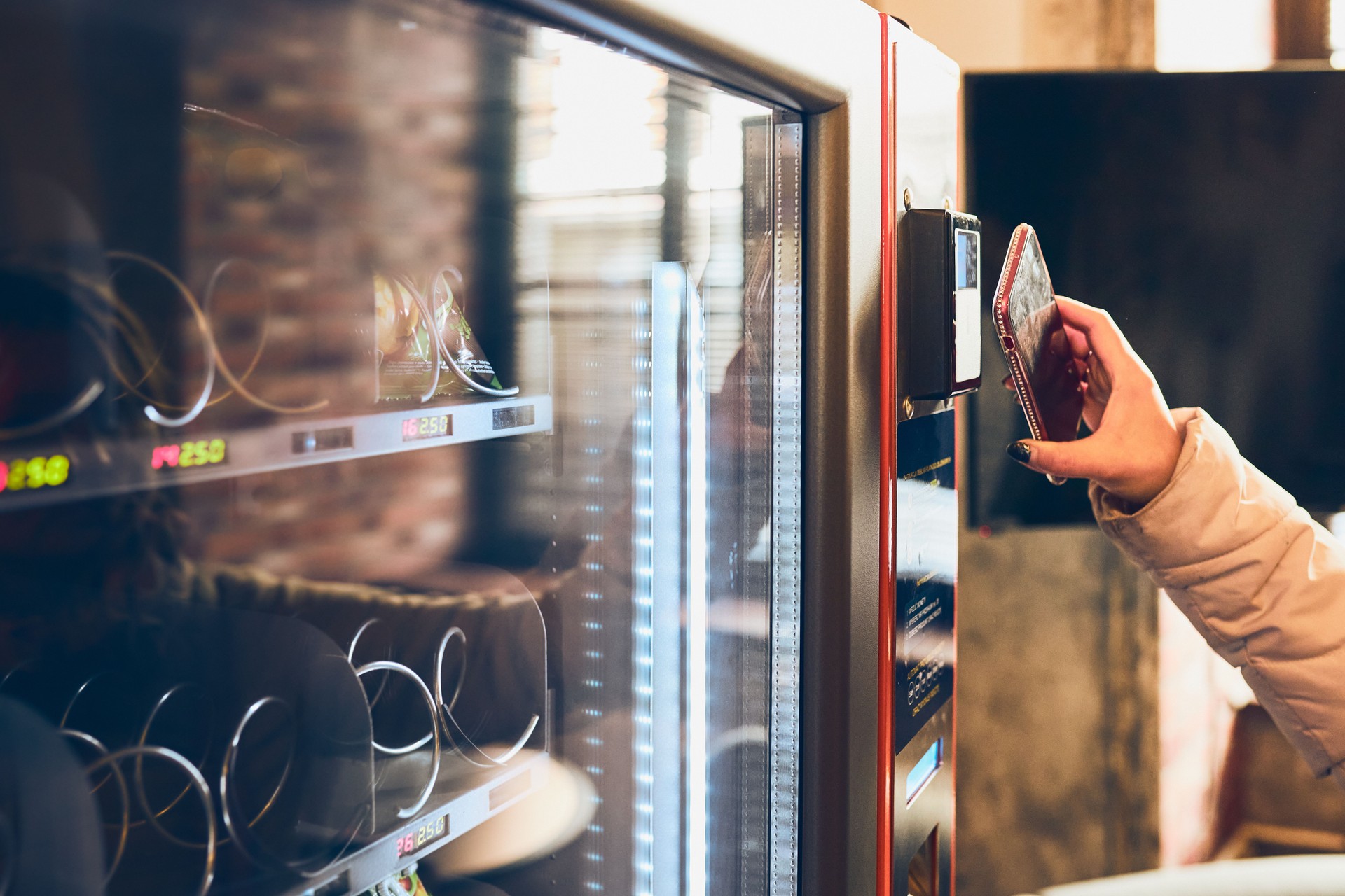 Woman Paying For Product At Vending Machine Using Contactless Method Of Payment With Mobile Phone